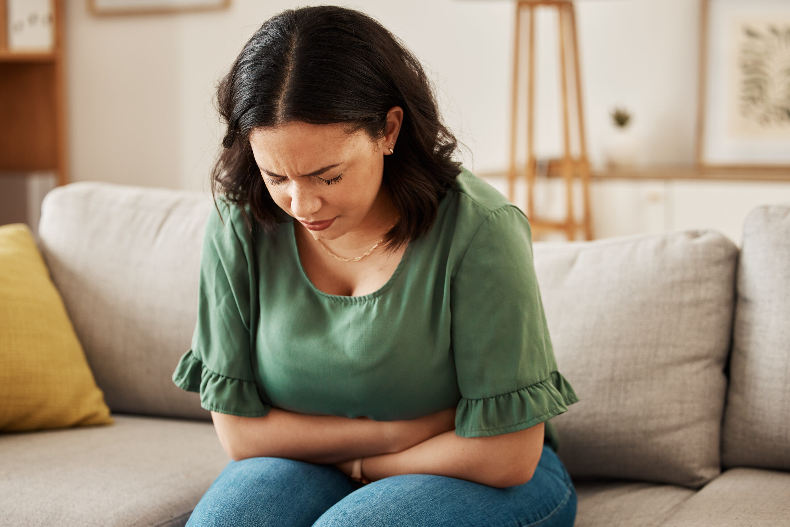 Stress, stomach pain and woman on a sofa with menstruation, gas or constipation, pms or nausea at home. Gut health, anxiety and lady with tummy ache in living room from ibs, bloated or endometriosis.